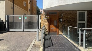 Une entrée fermée par un portail en métal, une porte en bois et une rampe menant à un bâtiment doté d’une balustrade en verre.