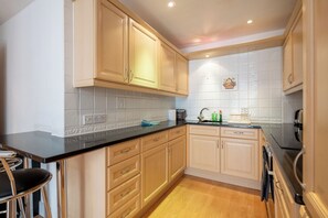 A kitchen with wooden cabinets, a black countertop, and a tiled backsplash. - Chic Central 2BDR London Retreat (Greater London)