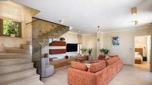 Ein modernes Wohnzimmer mit Treppe, einer Couch, einem Flachbildfernseher und einem Bild an der Wand.