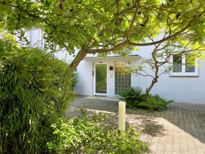 A building with a white exterior, a door with a glass panel, and a small garden area with plants and a pathway leading to the entrance. - Holiday apartment SeeZeit2 - a cozy retreat for relaxation near the lake (Nonnenhorn)