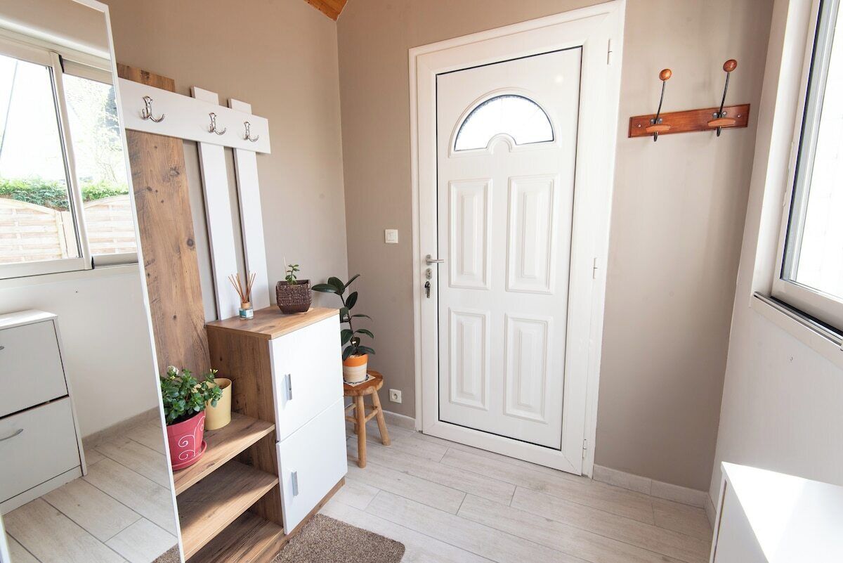 Una habitación con una puerta blanca, un estante de madera con adornos, un taburete pequeño y una planta en maceta.