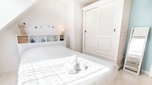 A bedroom with a bed, a wardrobe, a mirror, and a shelf with decorative items. - Family home with a veranda and large garden, 7 min from the beaches by Groom* (Guidel)