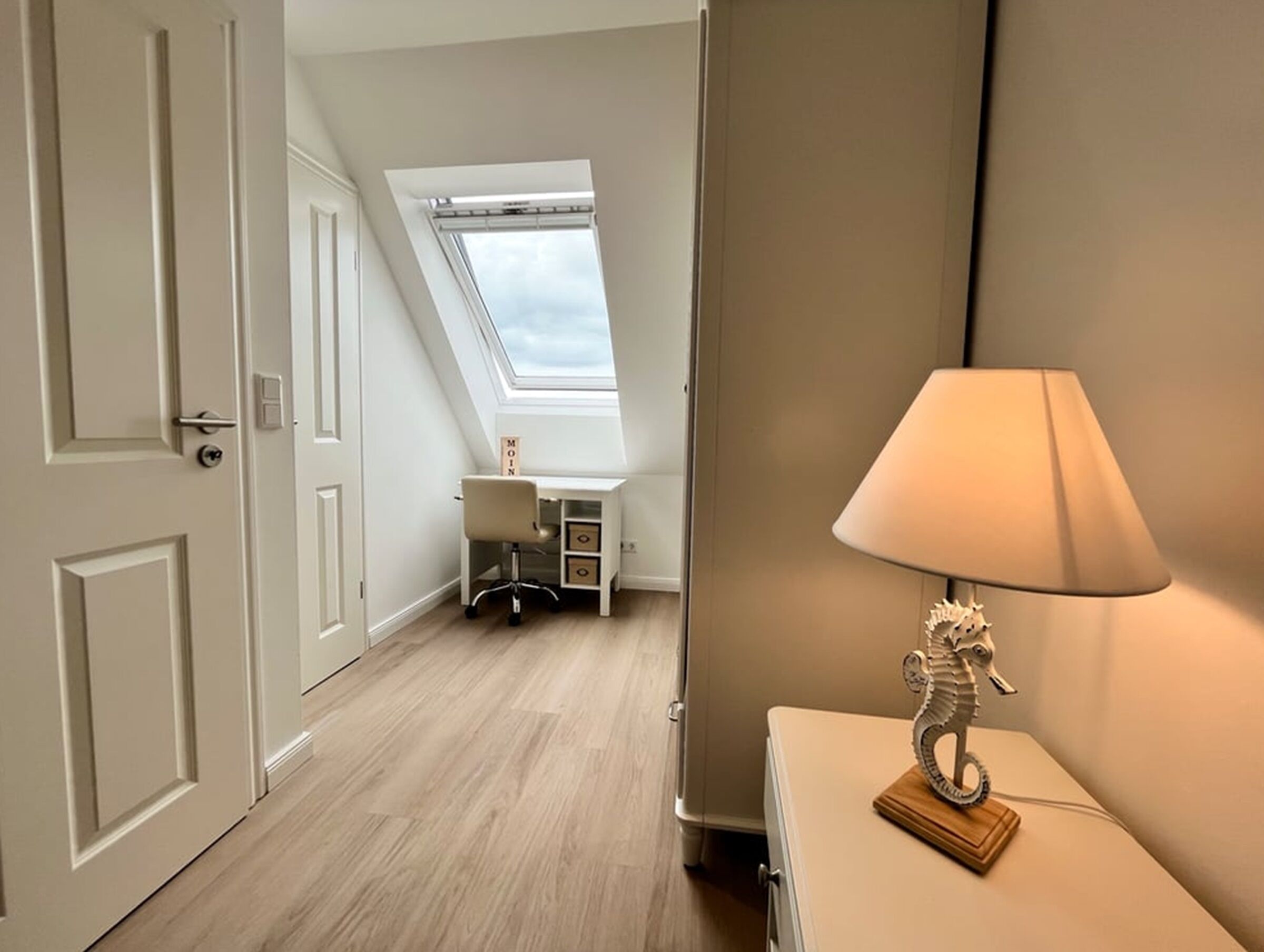 A room with a skylight, a desk, a lamp, and a dresser.