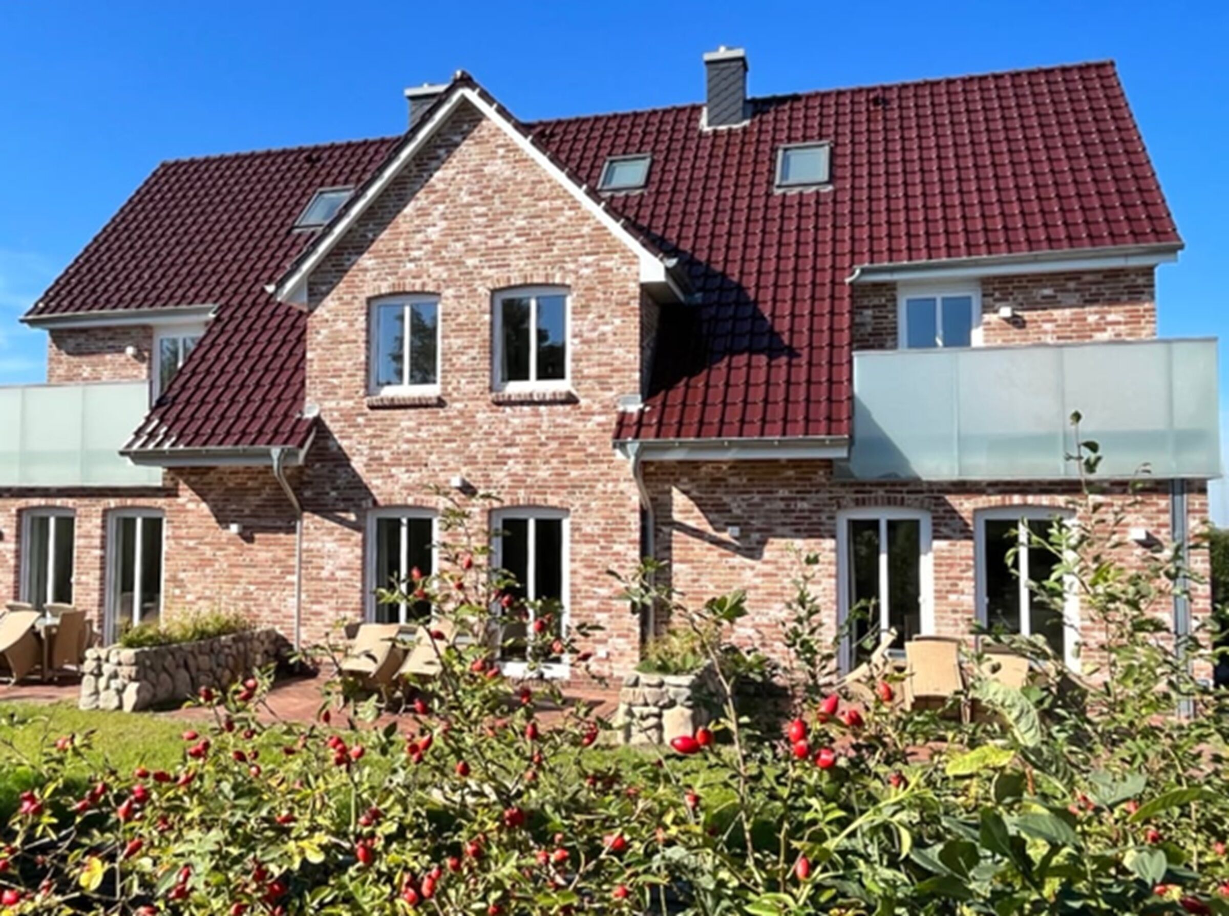 Ein zweistöckiges Haus mit rotem Ziegeldach, Backsteinwänden und einem Garten mit roten Beeren.