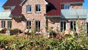 Ein zweistöckiges Haus mit rotem Ziegeldach, Backsteinwänden und einem Garten mit roten Beeren.