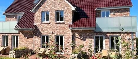 Une maison à deux étages, avec un toit recouvert de tuiles rouges, des murs en briques et un jardin où poussent des baies rouges.