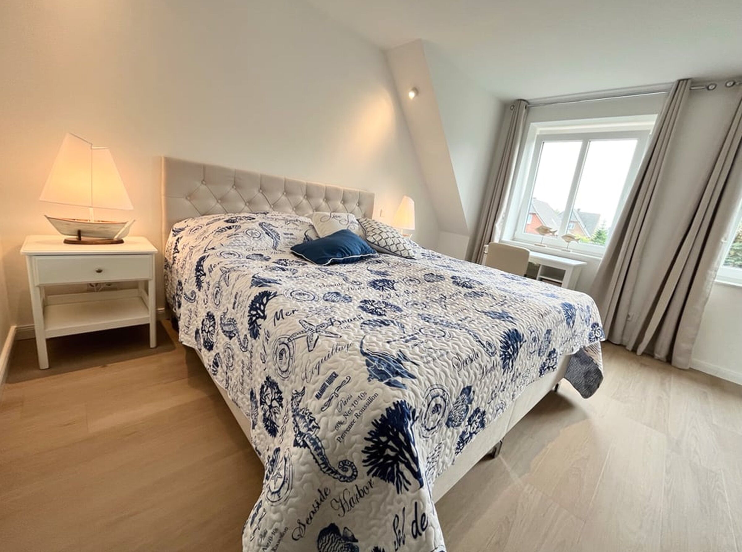 Ein Schlafzimmer mit einem Bett, Nachttischen, einem Fenster und Blick ins Freie.