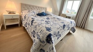 Ein Schlafzimmer mit einem Bett, Nachttischen, einem Fenster und Blick ins Freie.