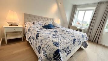 Ein Schlafzimmer mit einem Bett, Nachttischen, einem Fenster und Blick ins Freie.