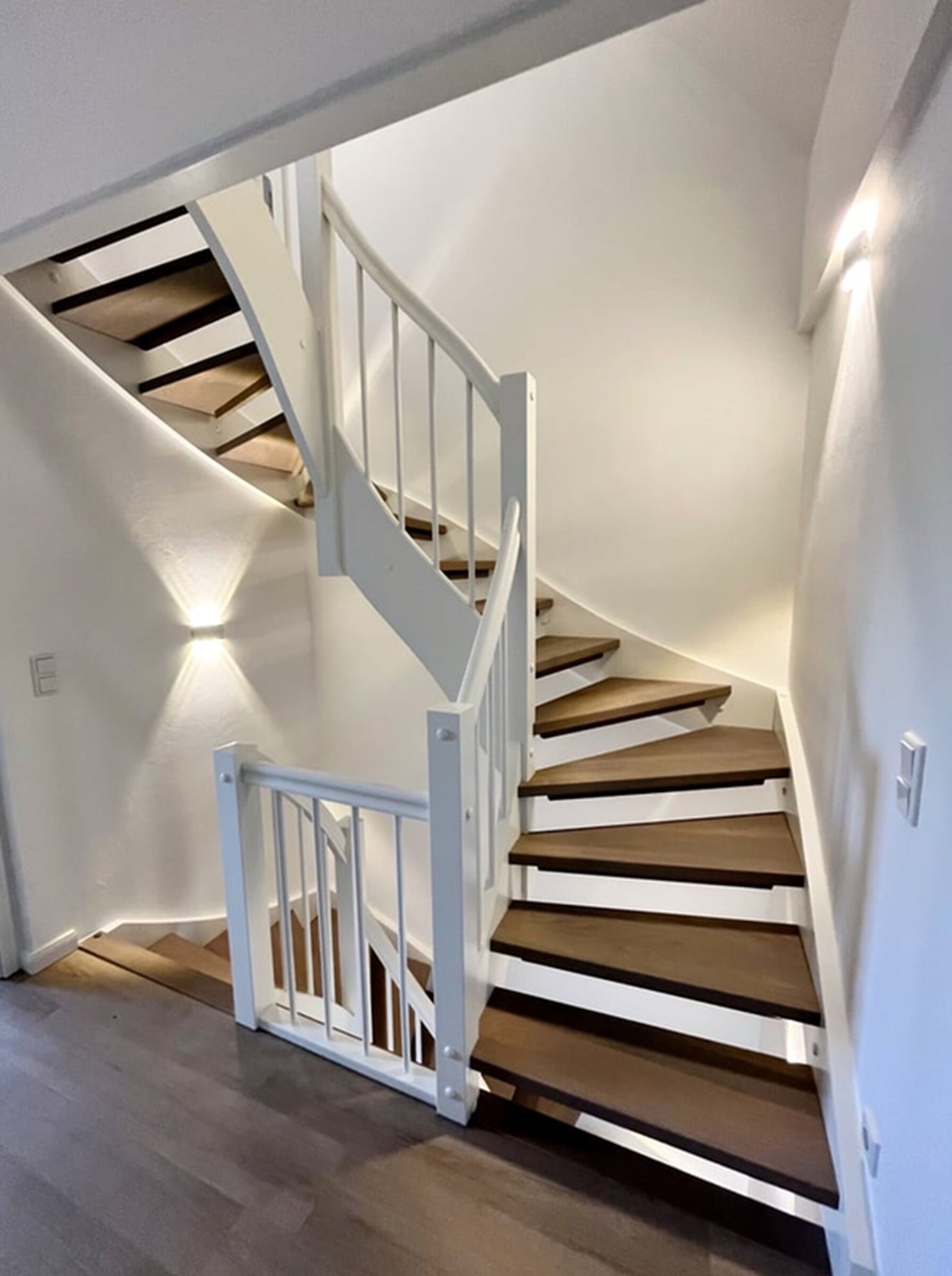 Eine Wendeltreppe mit weißen Geländern und Holzstufen, die zu einer oberen Etage führt.