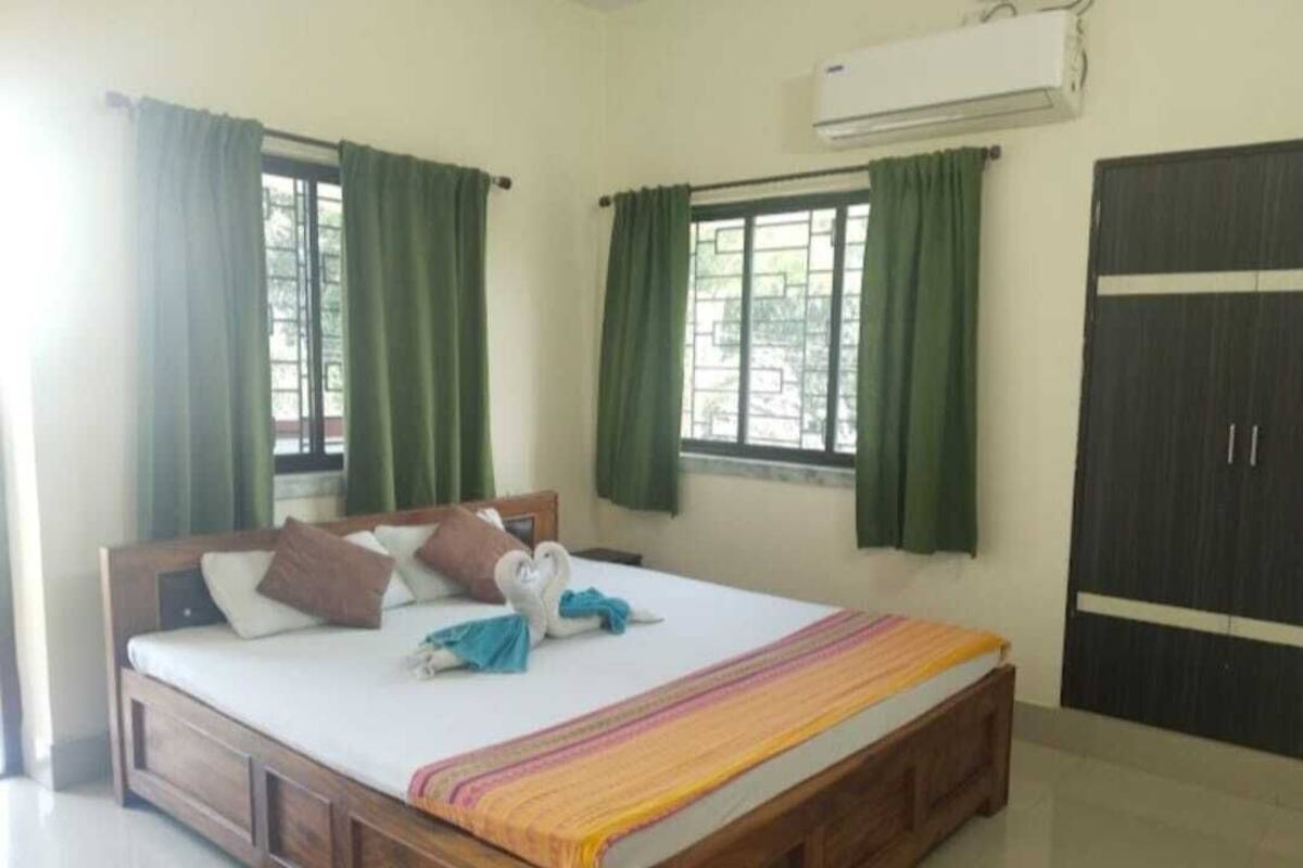 Un dormitorio con cama de madera, cortinas verdes, una ventana y un equipo de aire acondicionado.