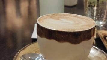 A cup of coffee with a spoon on a wooden coaster, a glass of water, and a green cushioned bench in the background.