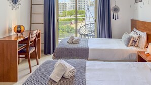 Ett hotellrum med två sängar, ett skrivbord, en stol, en hängstol och utsikt över byggnader genom fönstret.