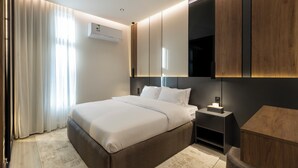 Una habitación de hotel moderna con una cama grande, mesitas de noche, un armario y un equipo de aire acondicionado.
