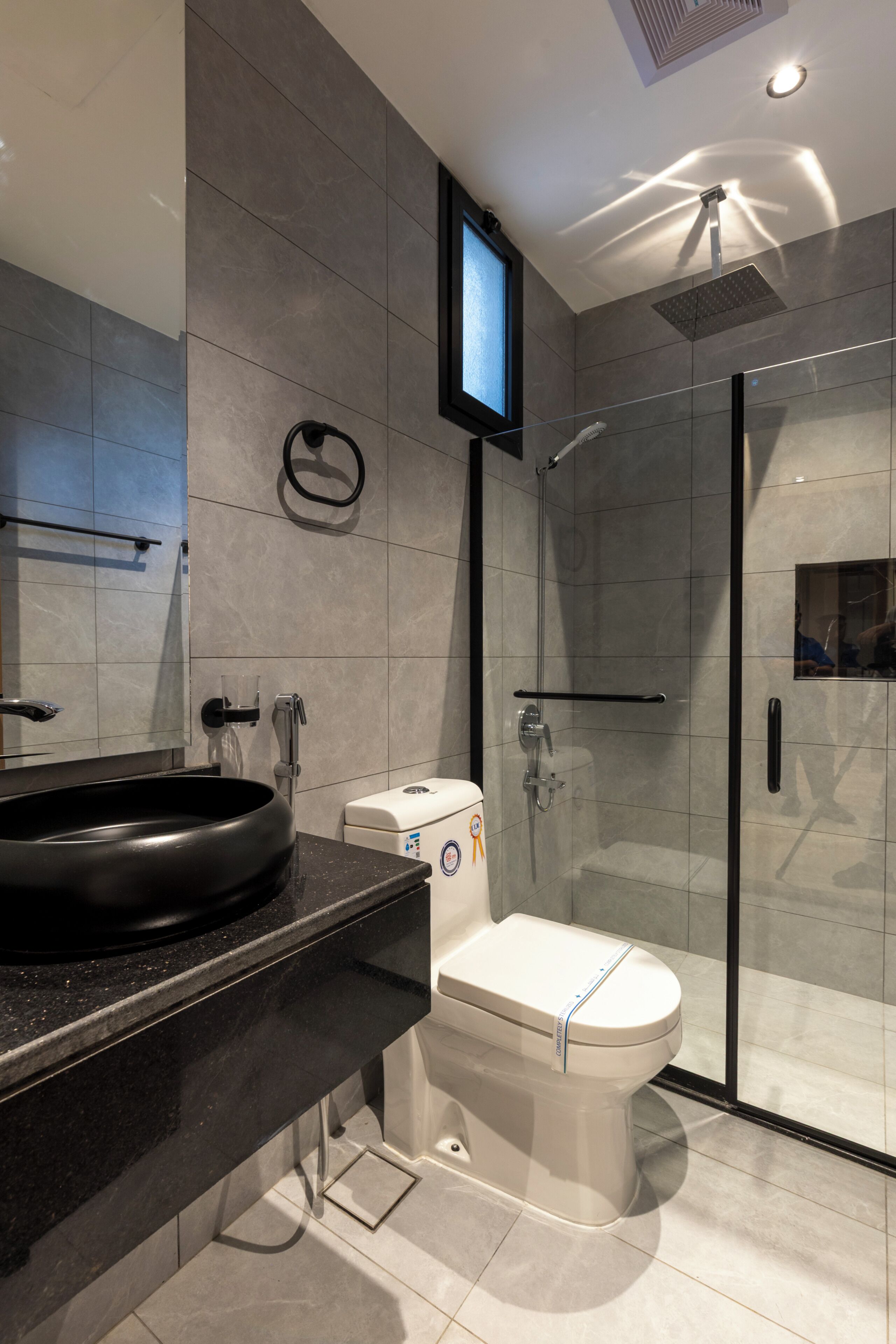 Un baño moderno con cabina de ducha de vidrio, un lavamanos negro y un inodoro.
