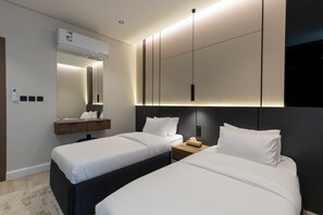 Une chambre d’hôtel moderne avec deux lits, un système de climatisation intégré, une table de chevet avec une lampe et un grand miroir au-dessus du lit.