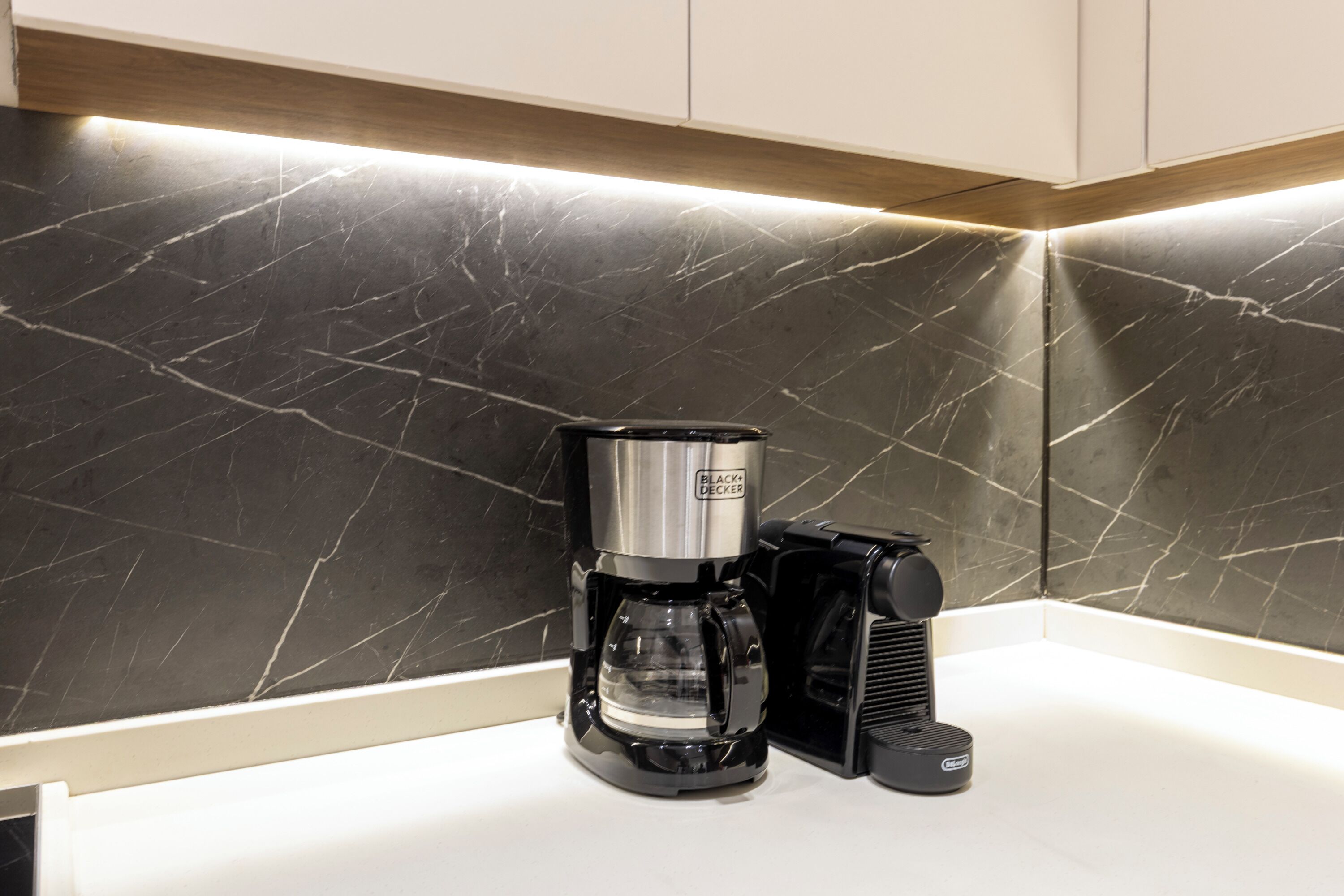 A coffee maker on a countertop with a marble backsplash.