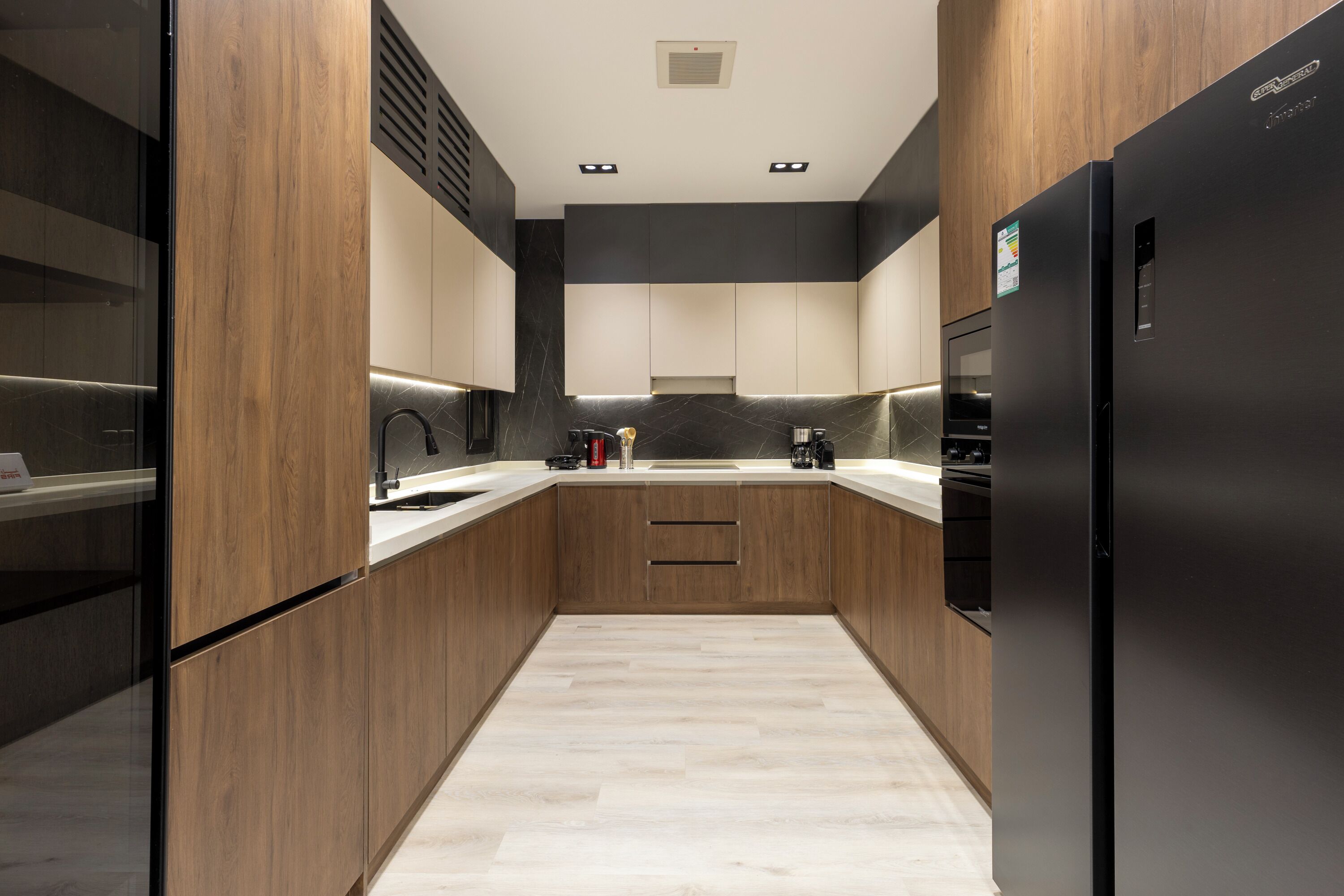 Une cuisine moderne avec des meubles en bois, un réfrigérateur noir et un plan de travail de couleur claire.