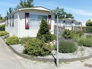 Ein Mobilheim mit einem Schild 'Hartogvliet', umgeben von angelegten Gärten und einem gepflasterten Zufahrtsweg.