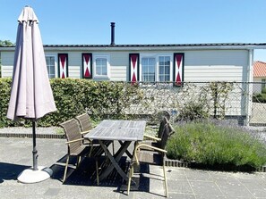 Eine Terrasse mit Tisch und Stühlen, einem Sonnenschirm und einem Haus mit roten und weißen Fensterläden.