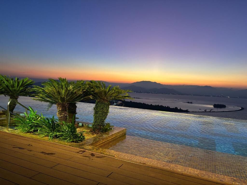 Ein Infinity-Pool mit Blick auf einen Sonnenuntergang über Wasser und Bergen.