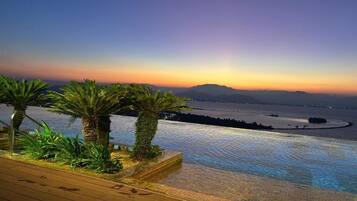 Ein Infinity-Pool mit Blick auf einen Sonnenuntergang über Wasser und Bergen.