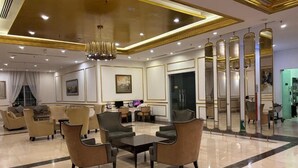 A spacious lobby with a high ceiling, a chandelier, seating area with sofas and armchairs, and a reception desk. - Golden Bay 2 Bedrooms Apartment (Da Nang)