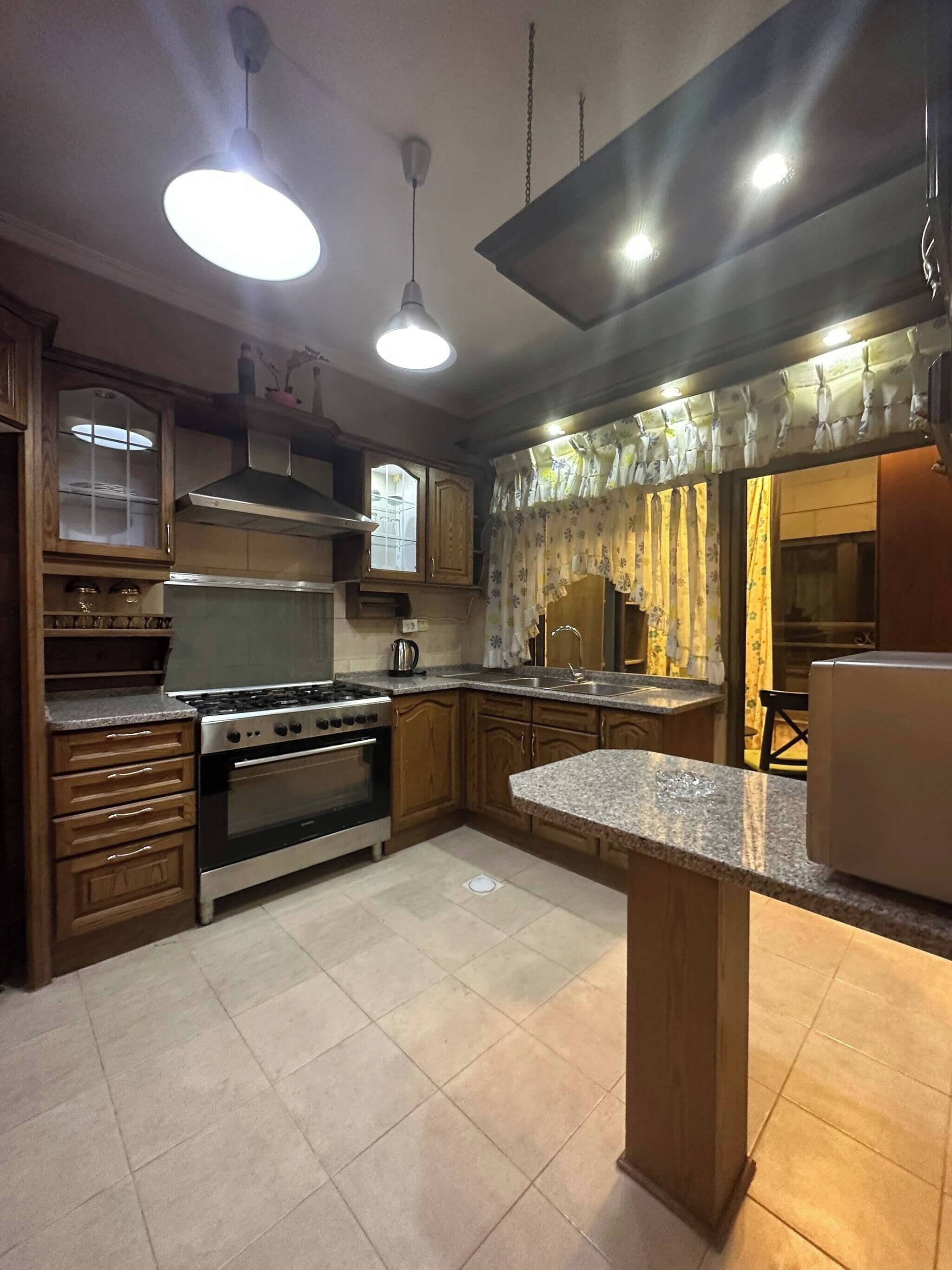 A kitchen with a central island, stainless steel appliances, wooden cabinets, and a window with curtains.