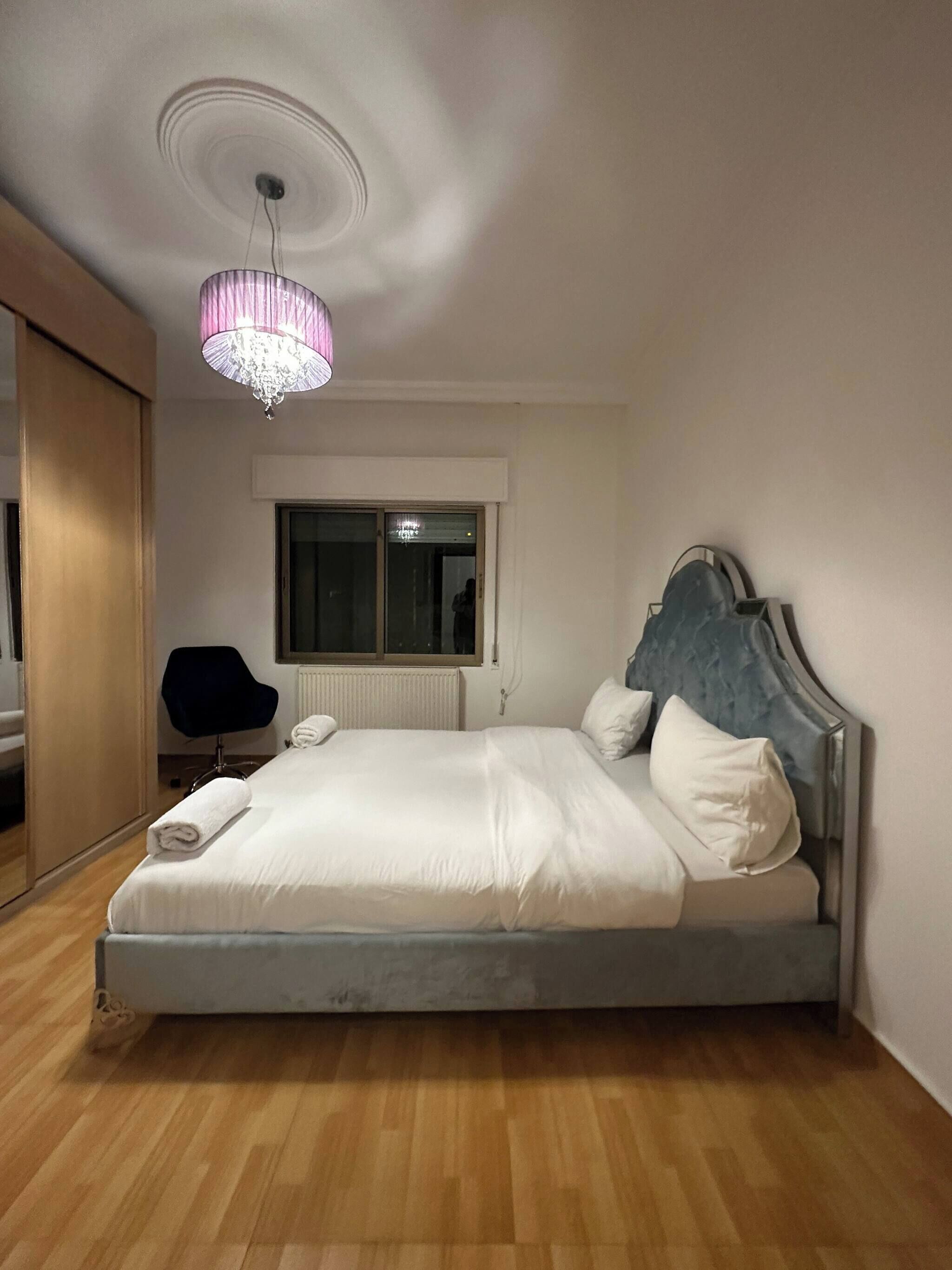 A bedroom with a bed, a chair, a window, and a chandelier.