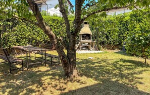 A garden with a stone barbecue area, a wooden bench, and a tree. - Nice apartment in Rijeka with house sea view (Rijeka)