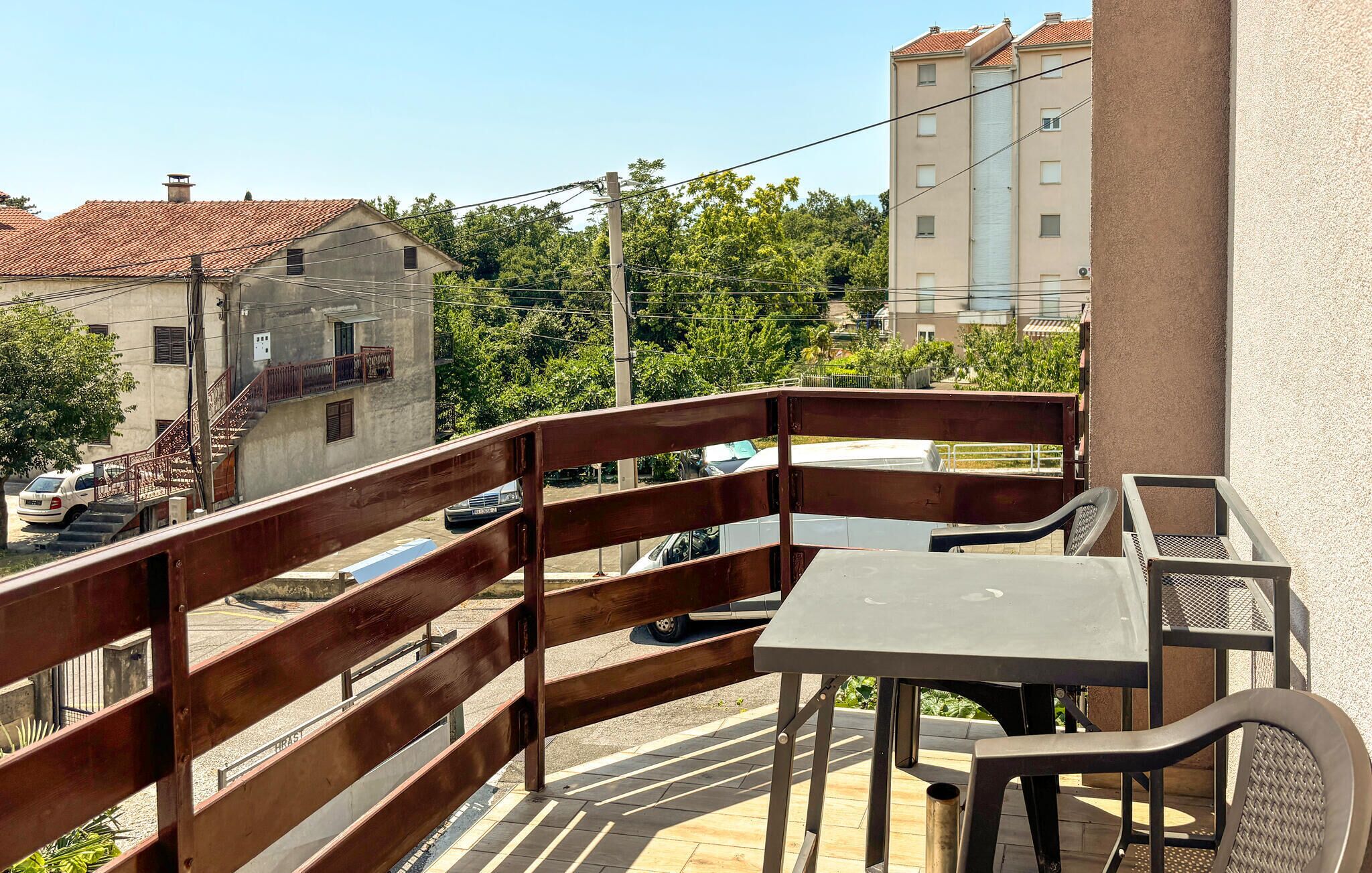 A balcony with a table and chairs, a wooden railing, and a view of buildings and trees.