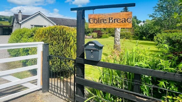 A wooden sign reading 'Coire Breac' above a gate, with a mailbox and a well-maintained garden in the background. - Coire Breac near Roy Bridge (Inverroy)