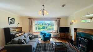 A living room with a sofa, armchair, fireplace, and a view of greenery outside. - Coire Breac near Roy Bridge (Inverroy)