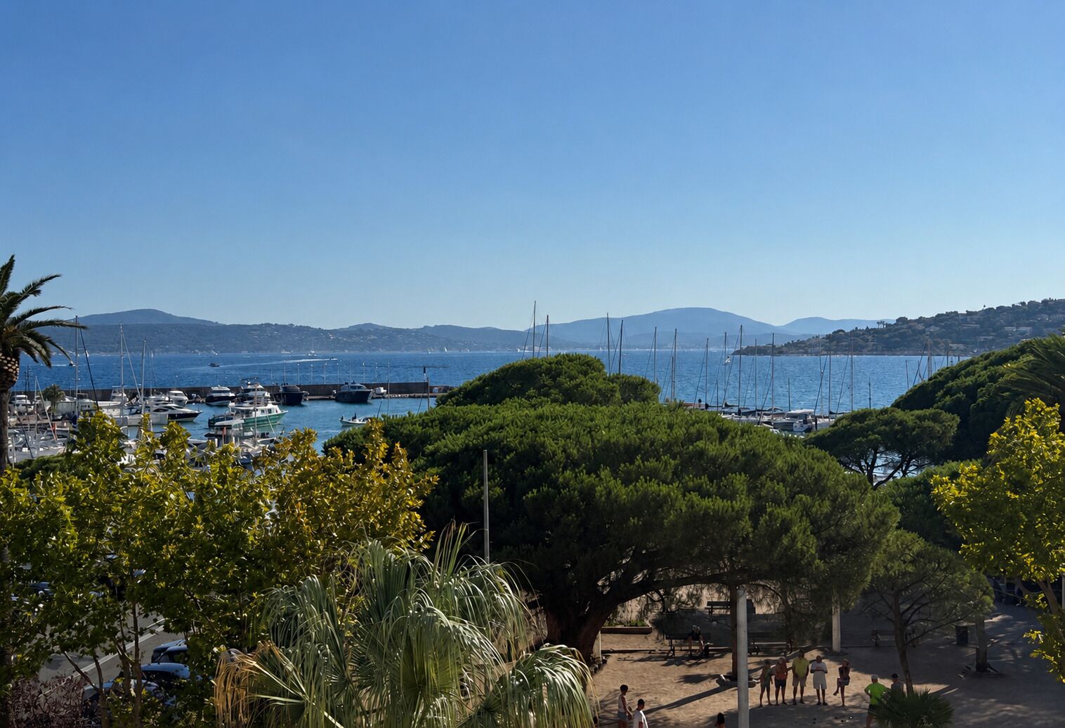 Un port de plaisance avec des bateaux, une plage de sable et un paysage montagneux en arrière-plan.