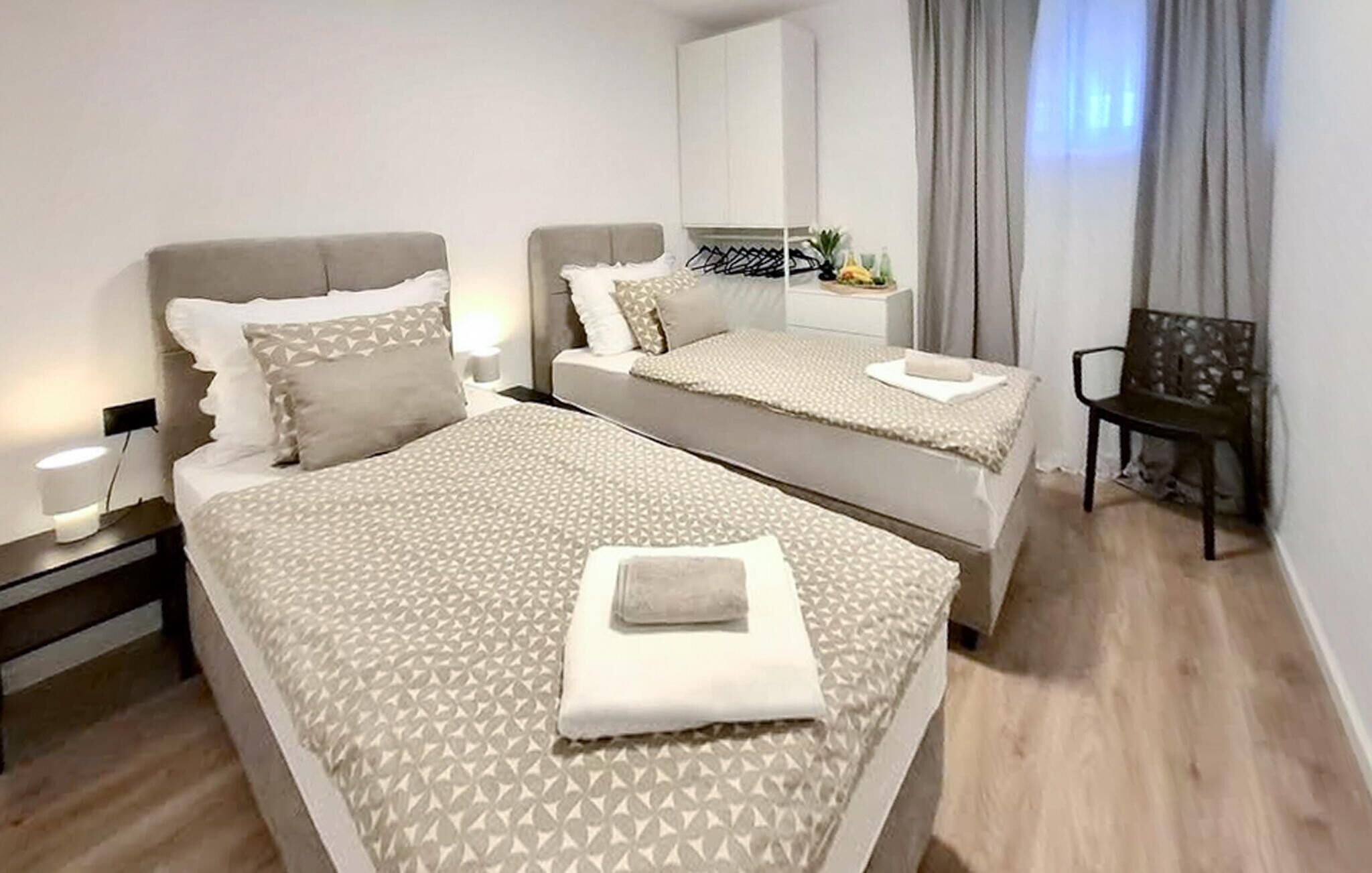 A modern hotel room with two beds, a desk, a chair, and a large window with curtains.