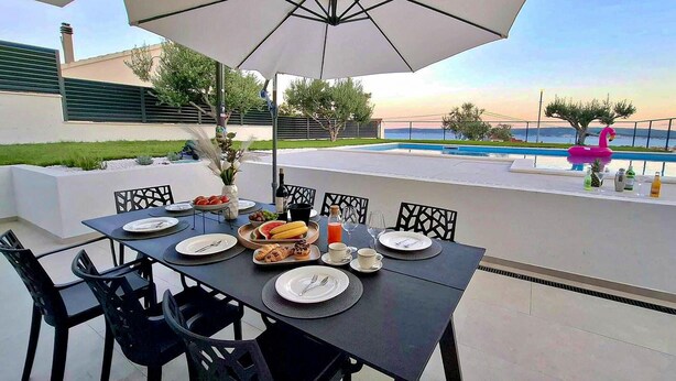 An outdoor dining area with a table set for four, surrounded by chairs, under a large umbrella. - Gorgeous home in Kastel Stari (Kastel Stari)