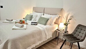 A neatly made bed with pillows, a bedside table with a lamp, a chair, and a small table with a vase and a book. - Gorgeous home in Kastel Stari (Kastel Stari)