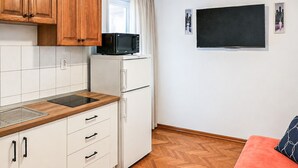 A compact kitchen with a microwave, a refrigerator, and a built-in oven. There is a white countertop, wooden cabinets, and a herringbone-patterned floor. A flat-screen TV is mounted on the wall. - Nice apartment in Mimice with WiFi (Mimice)
