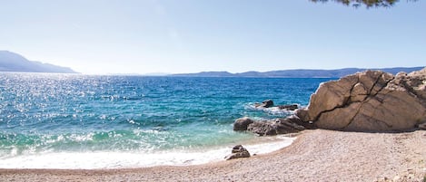 Uma praia rochosa com mar azul cristalino e montanhas ao longe.