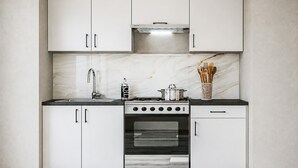 Cucina con mobili bianchi, cappa in acciaio inossidabile, piano cottura a gas, forno e schienale in marmo.