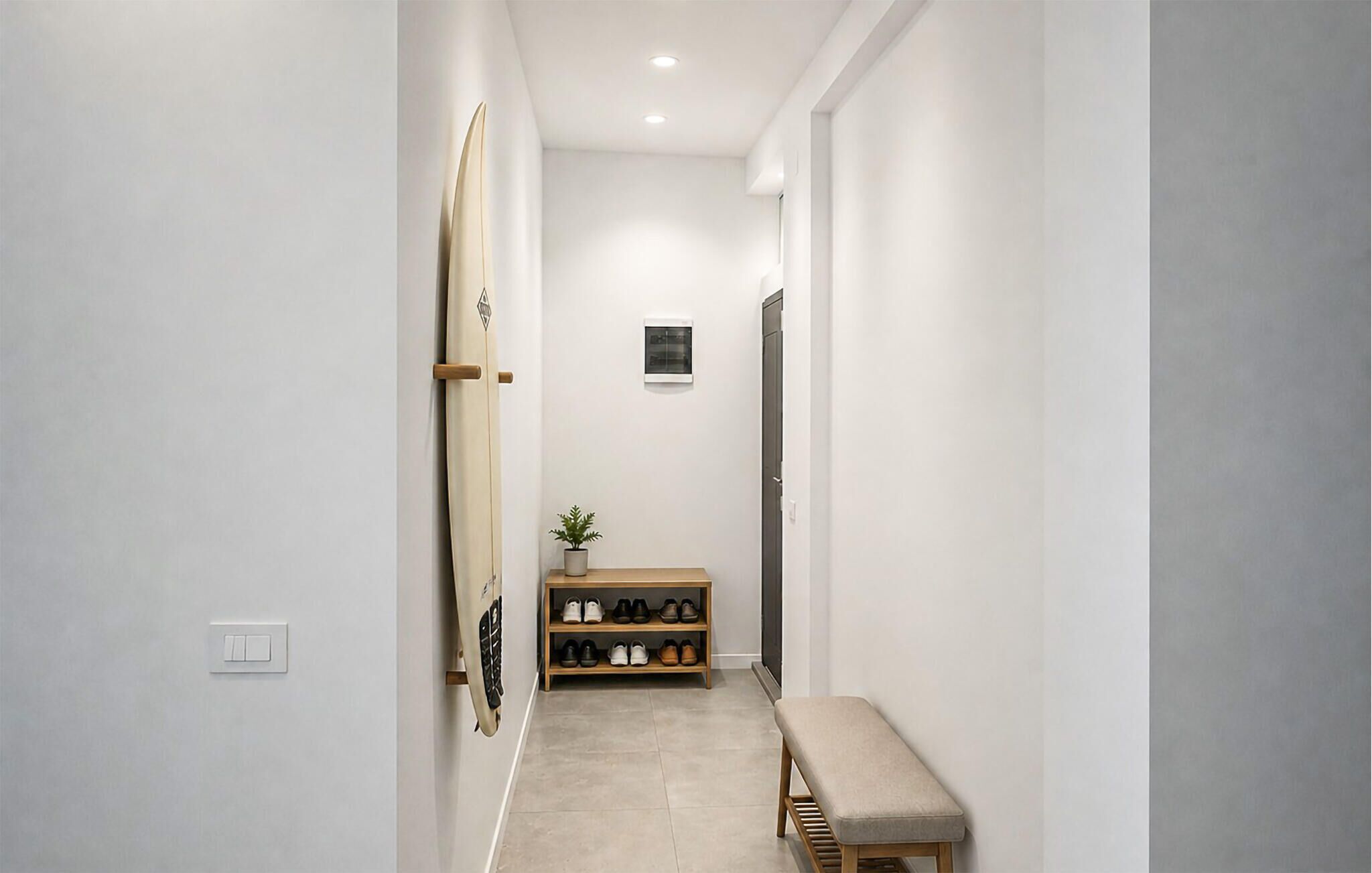 Ein Flur mit einer Bank, einem Schuhregal und einem Surfbrett, das an die Wand gelehnt ist.