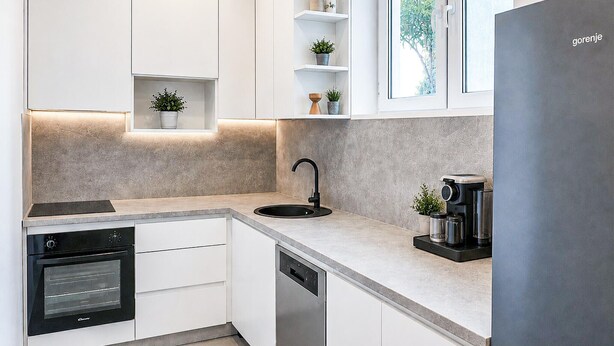 A modern kitchen with white cabinets, a built-in oven, a dishwasher, a black sink, and a coffee machine. - Lovely apartment in Mimice with WiFi (Mimice)