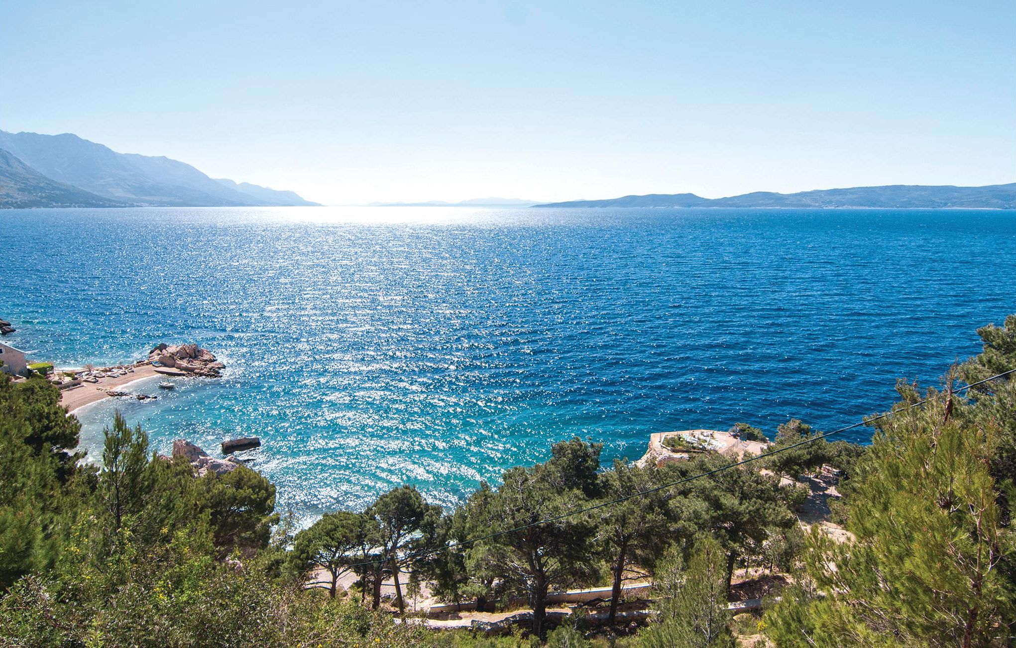 A coastal landscape with a clear view of the sea, rocky shoreline, and surrounding greenery.