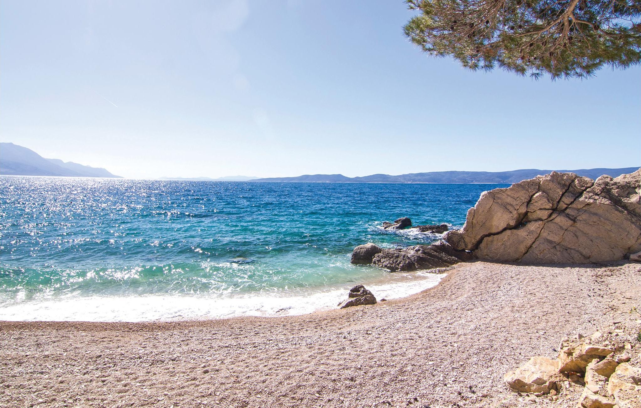 A rocky beach with clear blue sea and distant mountains.