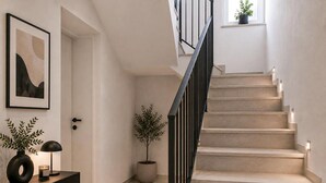 Una escalera de diseño moderno, una puerta con pomo decorativo, una obra de arte abstracta enmarco, una planta en maceta y un pequeño ventanal con plantas.