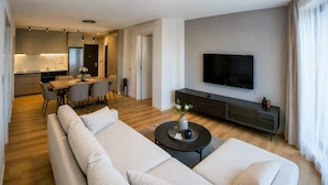 Una sala de estar moderna con sofá, una mesa de centro, televisor y una zona de comedor con sillas y una mesa.
