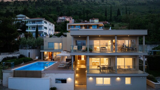 Una moderna casa a più piani con piscina, area relax esterna e vista sulle colline circostanti.