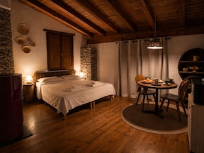 A cozy room with a bed, a round table with chairs, a stone wall, and a wooden ceiling.