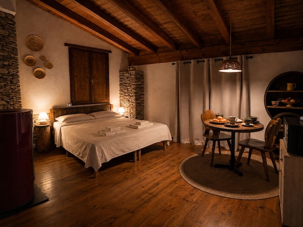 A cozy room with a bed, a round table with chairs, a stone wall, and a wooden ceiling.