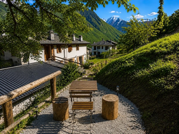 A wooden deck with a table and benches, surrounded by gravel, leading to a house with a sloped roof.